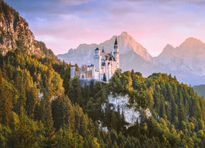 Een kasteel verscholen in een bebost berglandschap bij zonsondergang, omringd door de betoverende toppen van Beieren, roept de perfecte vakantiesfeer op.